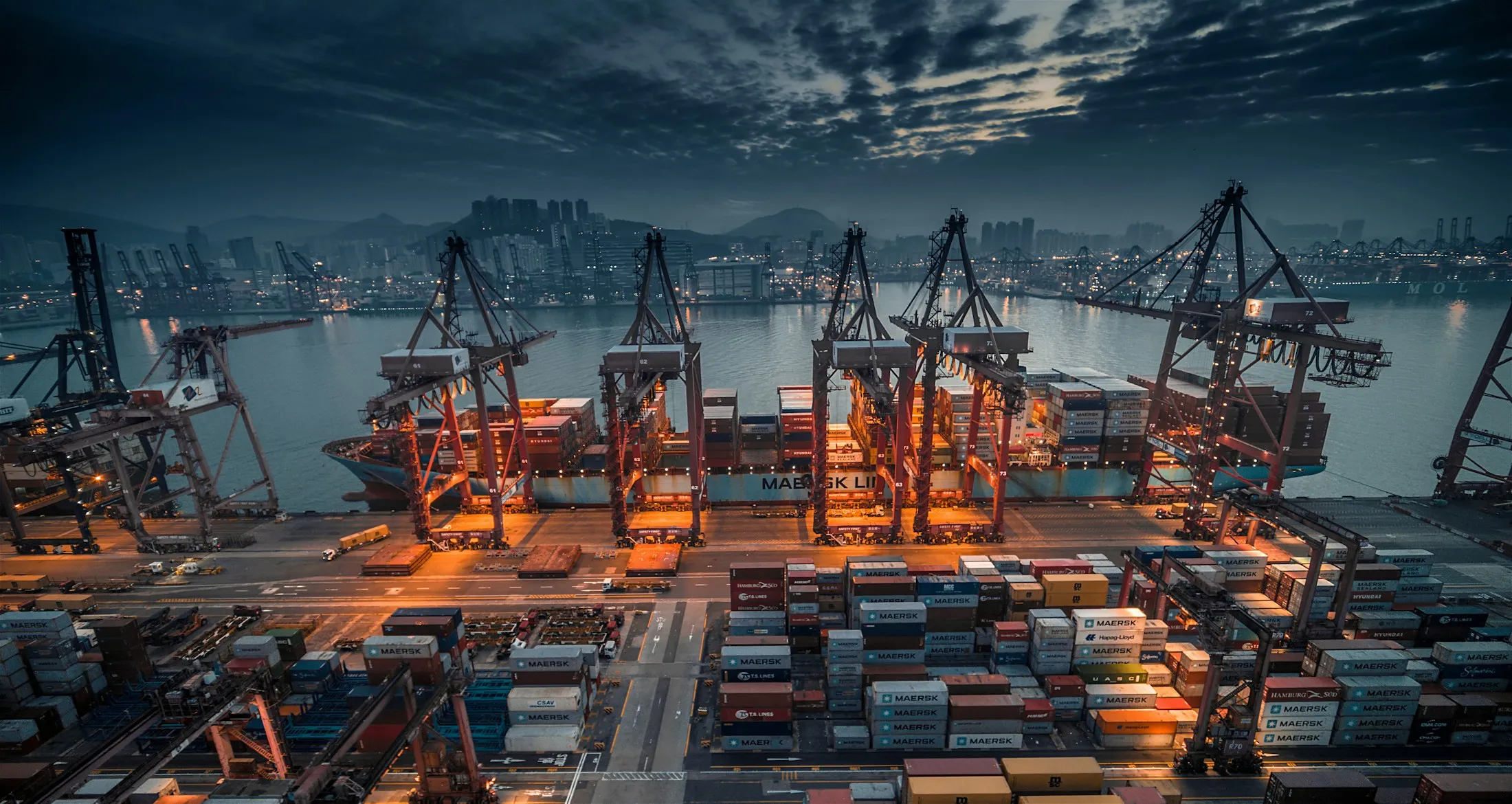 Gantry cranes working a container terminal at dusk.