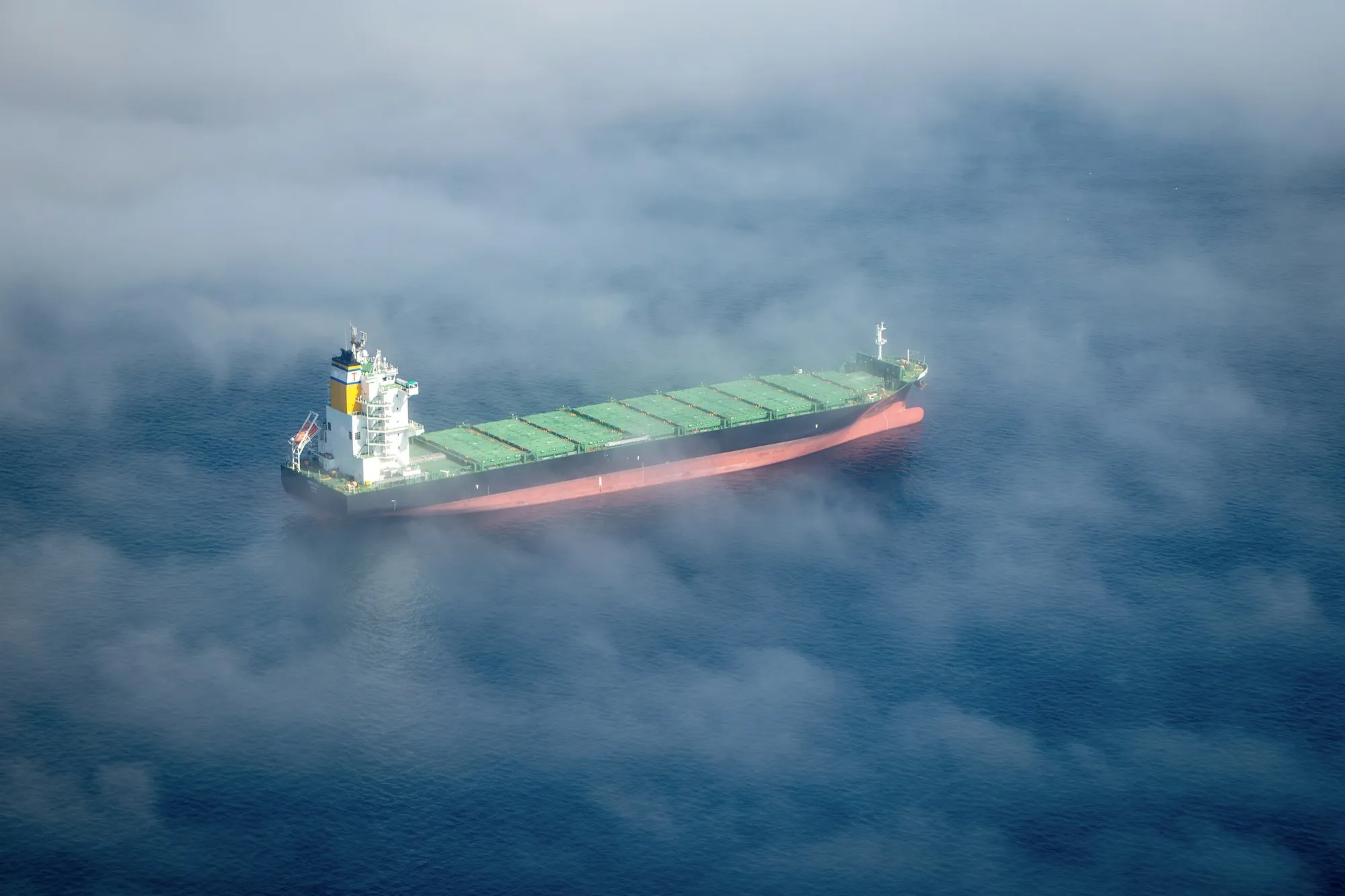 A container vessel under way, seen from above through heavy fog.